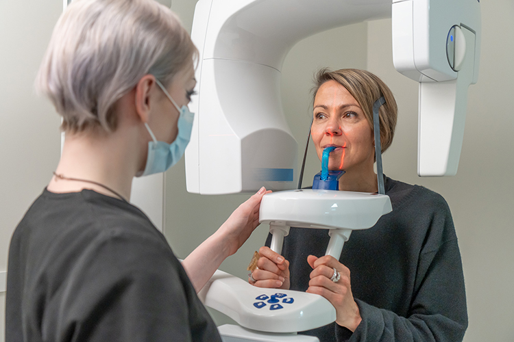A dental imaging professional positions a patient inside an OPG scanner using a bite block and head supports.