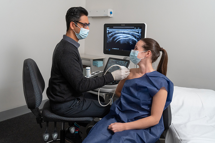 A sonographer performs an ultrasound examination on a patient’s shoulder using a handheld transducer.