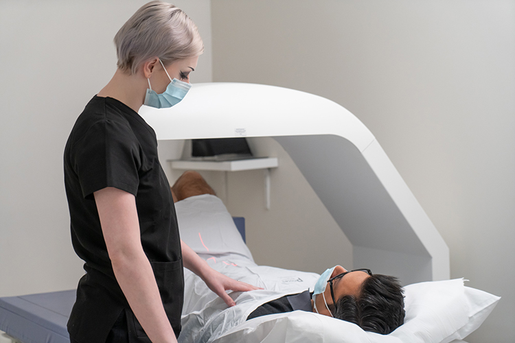 A radiographer monitors a patient lying on a bone densitometry scanner table during a scan.