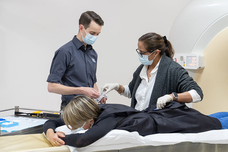 Clinical staff prepare a patient lying on an examination table for an interventional radiology procedure.