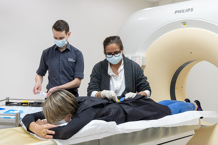 A doctor administers an image‑guided injection to a patient’s lower back while the patient lies on an CT bed.