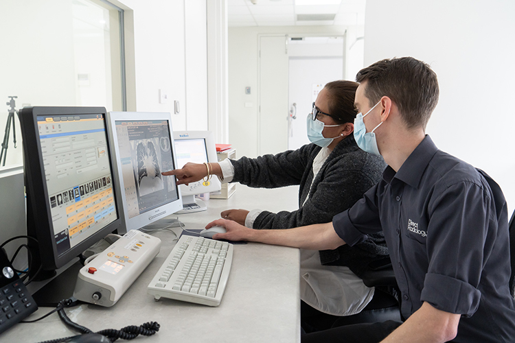 Two radiology professionals review medical imaging on computer monitors at a diagnostic workstation.